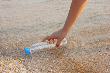 woman's hand collects plastic bottle on beach background. cleaning up beach. picking up plastic water bottle from the sandy beach. 