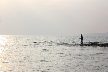 Naklejka premium Silhouette of man fishing on the beach at sunset.