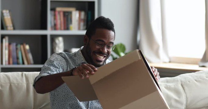 Excited african male customer receiving opening parcel box at home