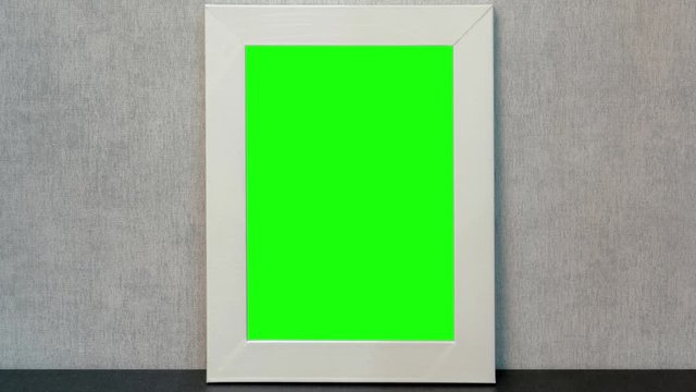 vertical photo frame with green chroma-key middle and white edges stands on black table against grey wall close view