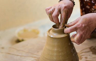 Hands of a potter make a vessel of clay on a pottery wheel. 
