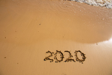 Fototapeta premium Summer beach holiday 2020 season golden sand - year - decade - new season lettering on the beach with wave and clear blue sea. Numbers 2020 year on the sea shore, message handwritten New Years concept