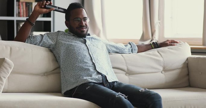 Happy african man hold remote control watching tv at home