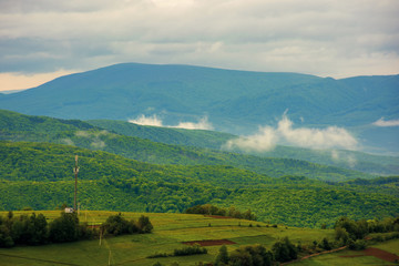 Fototapeta na wymiar clouds rising above the hills. mountainous countryside of carpathians. fog evaporate from the green forest just after it rains. overcast windy sunrise in springtime.