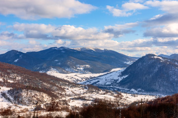 mountainous rural landscape on a sunny winter day. snow covered fields on hills. village in the distant valley. landscape with clouds on the sky