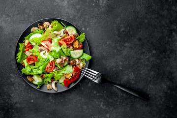 seafood salad, tomato, cucumber, sweet pepper, lettuce on a black plate on a stone background