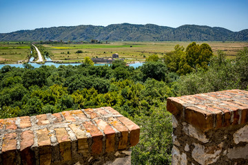 High angle sunny spring day view of salt lagoon lake, valley and mountain in the national park of Butrint in Albania, Europe. Blurred fort walls in the foreground.