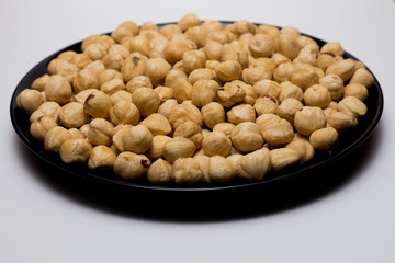 Whole hazelnuts in black plate on the white background. Healthy vegetarian snack. Close-up photo. Vegetable diet.