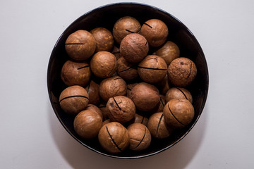 Whole macadamia nuts in black plate on the white background. Healthy vegetarian snack. Close-up photo. Vegetable diet.