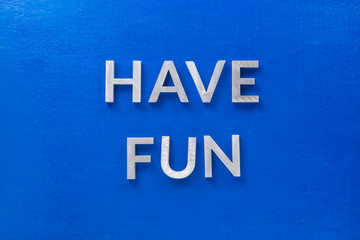 the words have fun laid with silver metal characters on blue painted wooden board in central flat...
