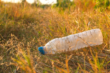 Garbage from plastic bottle that are thrown away on the dry grass ground with dry leaf which is a problem and pollution to the environment.
