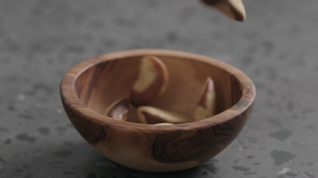 Slow motion brazil nuts falling into olive bowl on terrazzo countertop