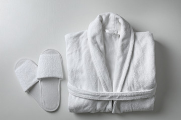 Clean folded bathrobe and slippers on white background, flat lay