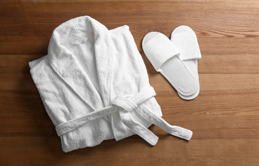 Clean folded bathrobe and slippers on wooden background, flat lay