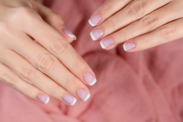 Closeup top view of two beautiful female hands with perfect professional french style classic manicure on fingernails. Healthy nails, skin and cuticle concept. Horizontal flatlay color photography.