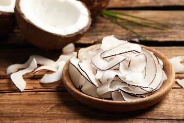 Delicious coconut chips in plate on wooden table