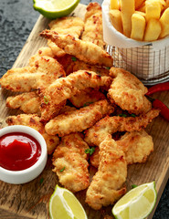 Buttermilk chicken nuggets served on wooden board with potato chips, lime wedges and tomato ketchup