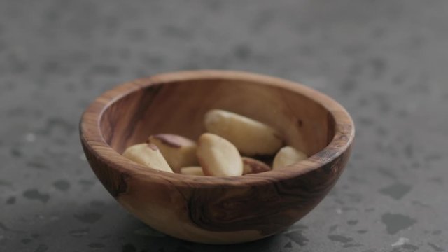Slow motion brazil nuts falling into olive bowl on terrazzo countertop