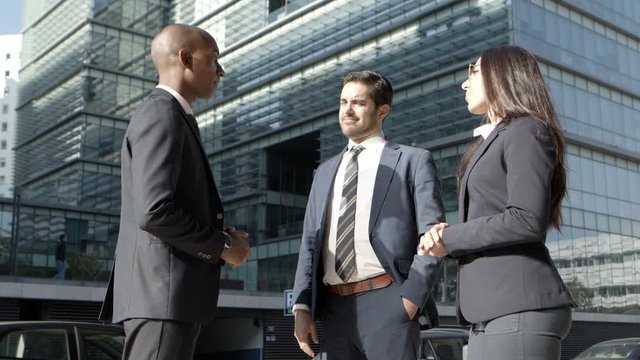 Content professional coworkers talking on street. Low angle view of multiethnic young businessmen and businesswoman discussing work while meeting on street. Business cooperation concept