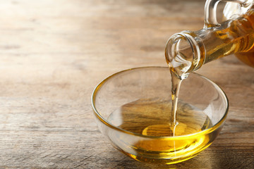 Pouring cooking oil from jug into bowl on wooden table