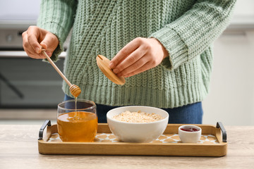 Woman adding honey to oatmeal at wooden table indoors, closeup