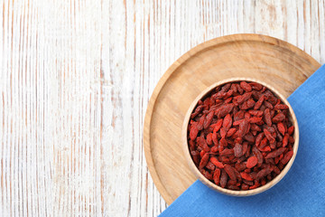 Obraz na płótnie Canvas Dried goji berries in bowl on white wooden table, flat lay. Space for text