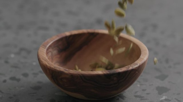 Slow motion dried pumpkin seeds falling into olive bowl on terrazzo countertop