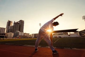 Obraz premium Full length portrait of a athletic man stretching at sport stadium.