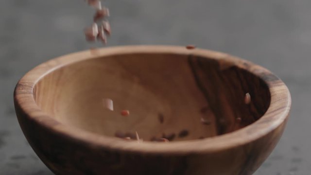 Slow motion flaxseed falling into olive bowl on terrazzo countertop