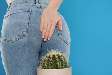 Woman sitting down on cactus against light blue background, space for text. Hemorrhoid concept