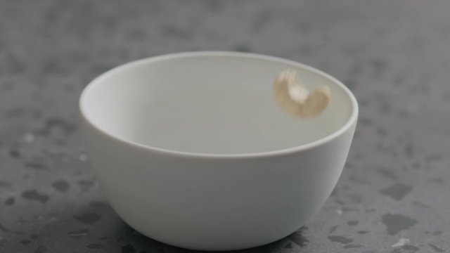 Slow motion dry cashew falling into white bowl on terrazzo countertop