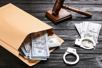Envelope with dollar bills and handcuffs on black wooden table. Bribe concept