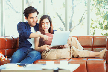 Fototapeta premium Excited young couple looking at laptop. Young couple watching media content online in a tablet sitting on a sofa in the living room.