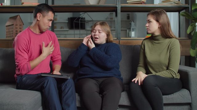 Positive young woman helping her hearing impaired diverse friends to order fast food by cellphone at home. Helping female with knowing of sign language ordering pizza by phone for deaf-mute people.