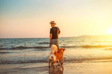 A man and a dog stand on the beach and sunset.