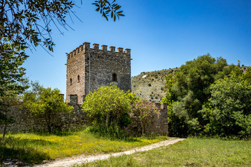 Fototapeta na wymiar The Tower with dusty path. Beautiful warm spring day and archeological ruins at Butrint National Park, Albania, UNESCO heritage. Travel photography with fresh green flora and clear blue sky