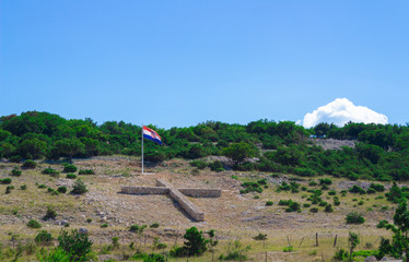 Stone Cross and flag on a mountain on the island of Krk. Croatia.
