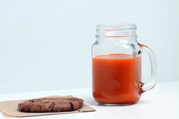 glass mug of carrot juice and a chocolate cookie isolated on white background