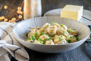 Fresh, just broiled homemade dumplings with green and butter in blue bowl on the dark wooden table. Country style concept.