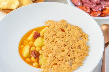 White modern plate with soup sauce of soybeans, sausage salami and potatoes, with cheese chips above closeup.