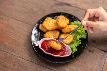 Chicken Nuggets impaled on a fork  and Dip sauce. A women eat Nuggets.