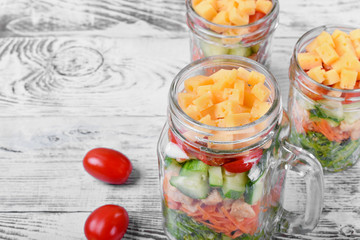 Layered salad with cheese, kale, carrot, chicken, cucumbers and cherry tomatoes in glass mason jars