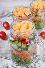 Layered salad with cheese, kale, carrot, chicken, cucumbers and cherry tomatoes in glass mason jars