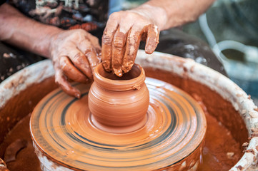 The potter makes pottery dishes on potter's wheel.