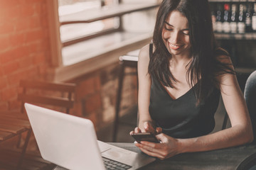 Business woman working on a laptop and using phone in a cafe.