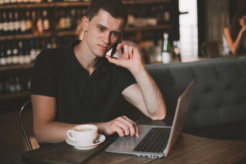 Businessman working on a laptop and using phone in a cafe.