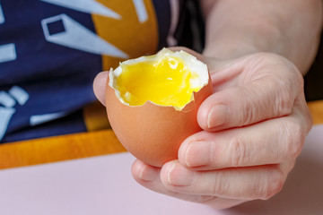 Opened egg with liquid yolk in the female hand close-up