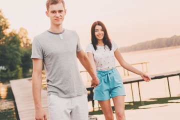 Loving young couple walking on pier at sunset in summer.