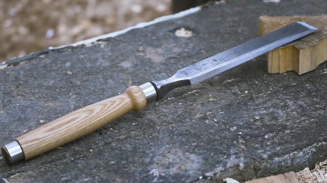 Close up of chisel with wooden handle lying on flat stony surface at the construction site. Clip. Professional equipment and woodworking concept.
