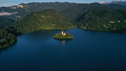 Aerial view of small island with Church of assumption of Mary in the middle of Lake Bled, Slovenia. Summer. Green Mountains landscape around lake.